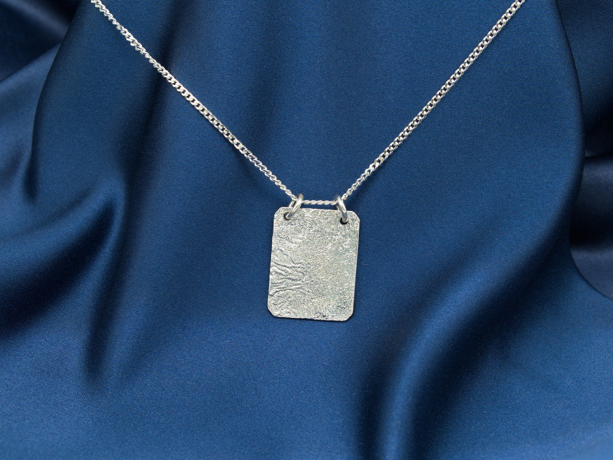 A sterling silver reticulated rectangular pendant suspended from a silver chain