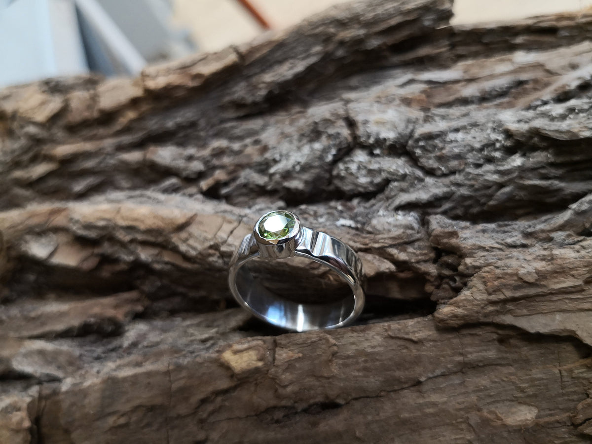 Reflective sterling silver ring with 6mm green peridot gemstone on a tree bark background